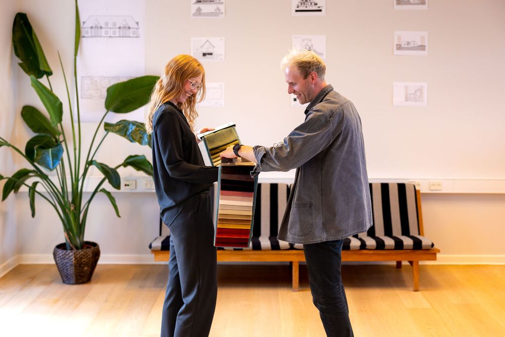 Two professionals reviewing fabric swatches together in a modern office with a striped bench and plant.