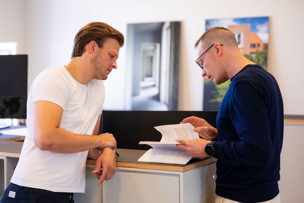 Two men reviewing documents together at a standing desk in a modern office environment.