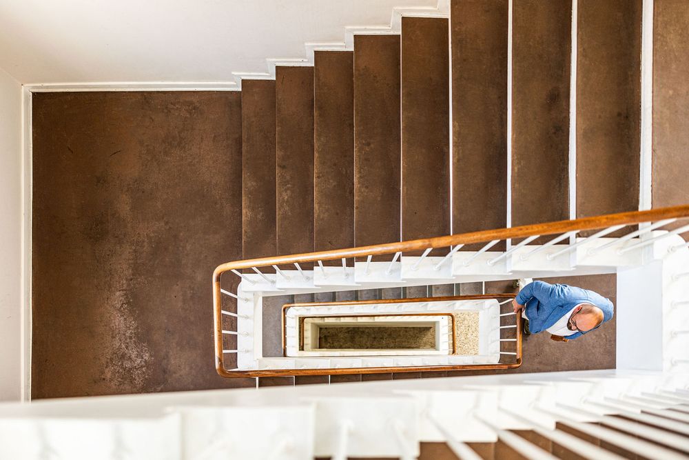 Aerial view of a spiral staircase with brown steps and white railings, with a person walking at the bottom.