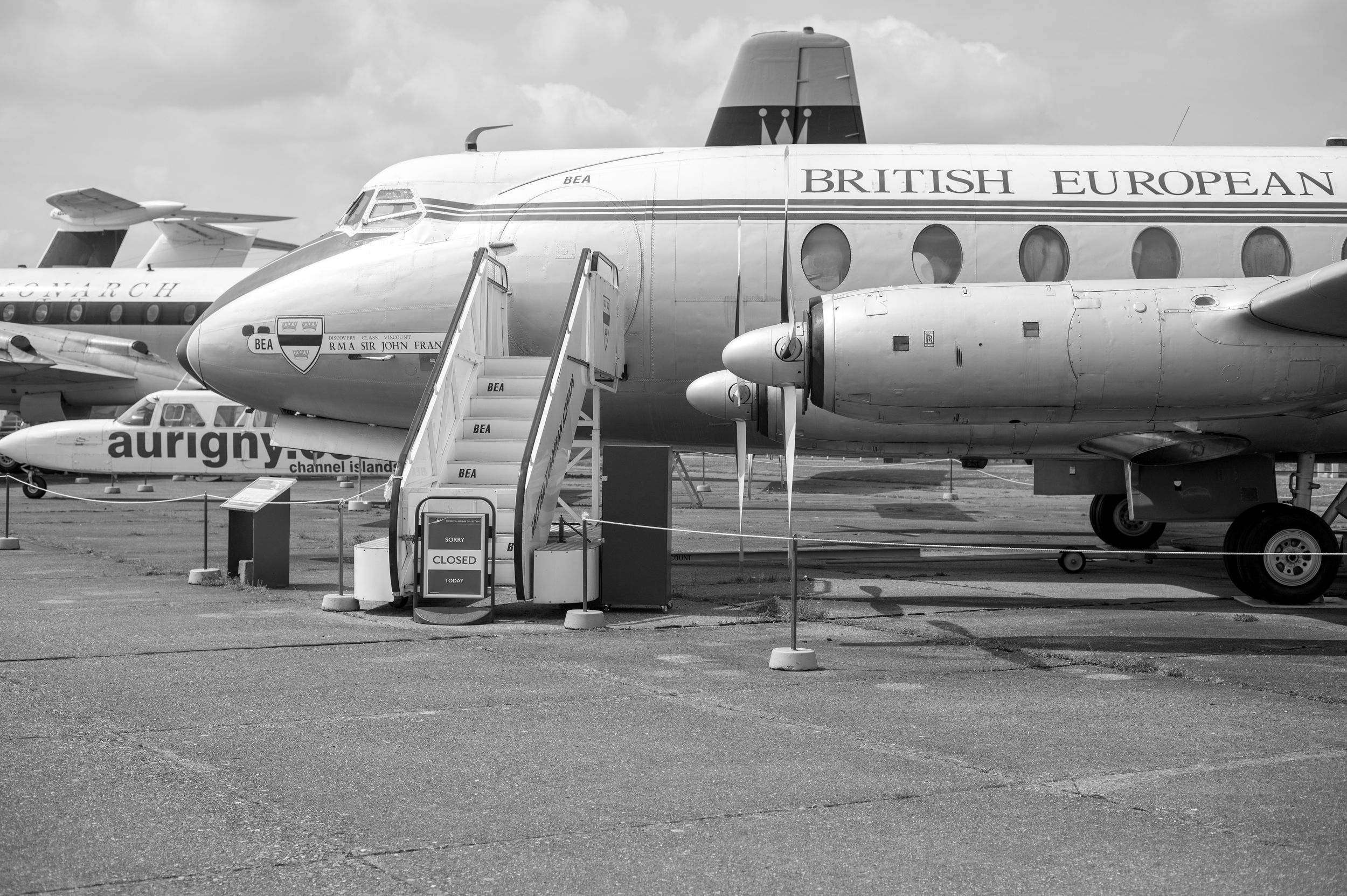 Vintage black and white photo of a British European Airways propeller aircraft on tarmac with boarding stairs attached.