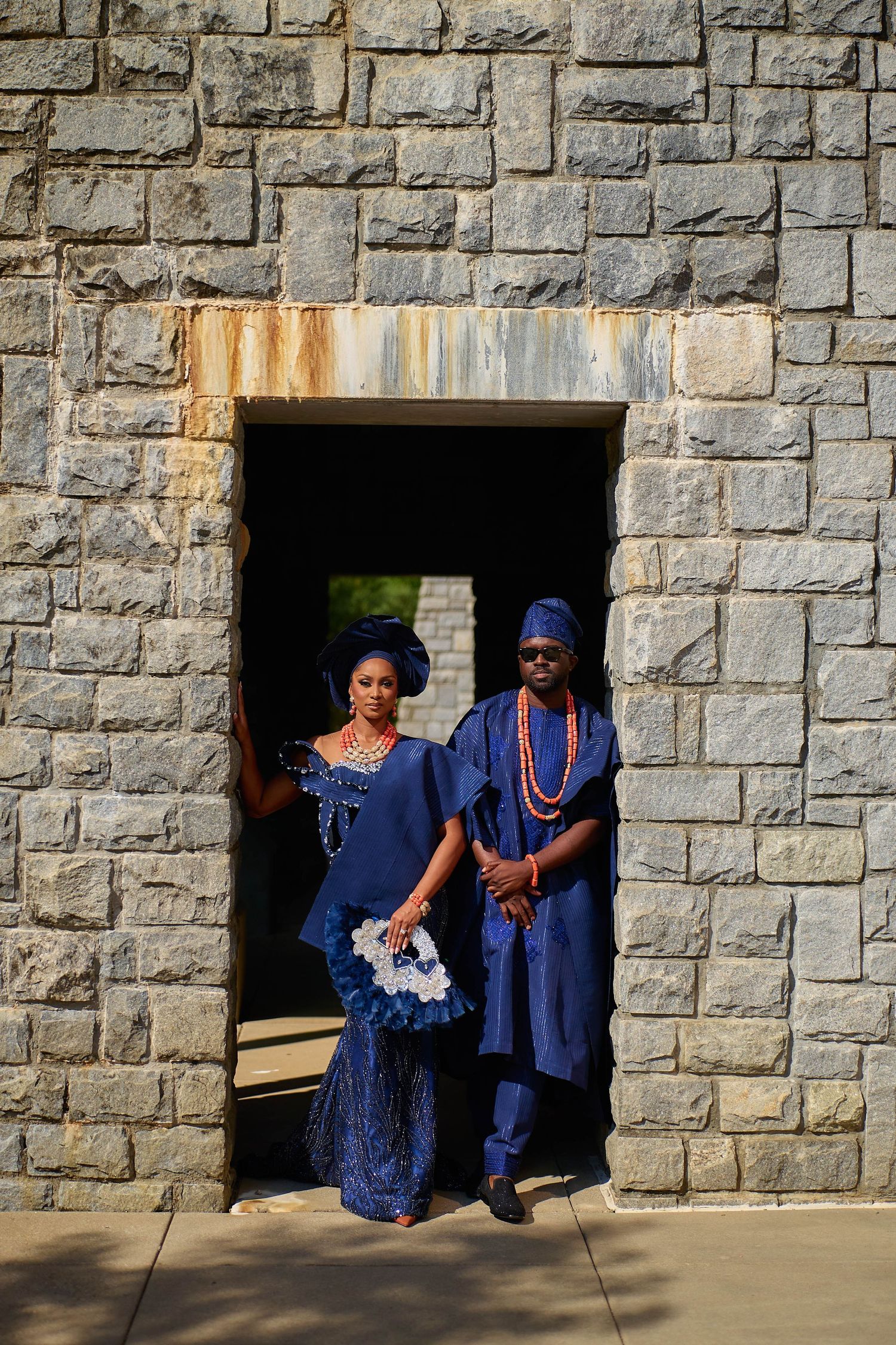 Couple in matching royal blue Nigerian traditional attire posing in stone archway doorway.
