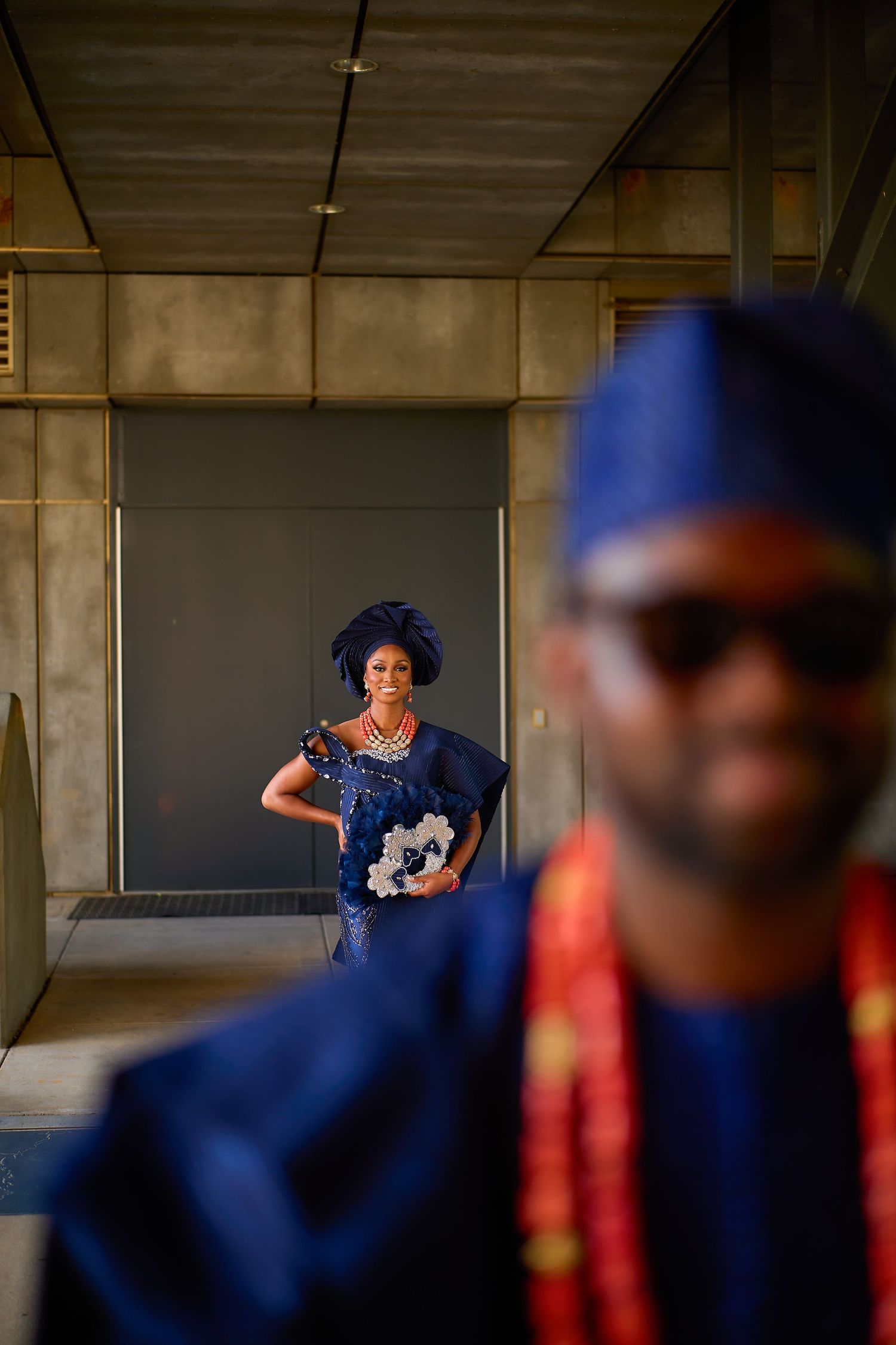 Nigerian couple in matching royal blue traditional attire, woman in embroidered gown and gele headwrap, man in agbada and fila cap.