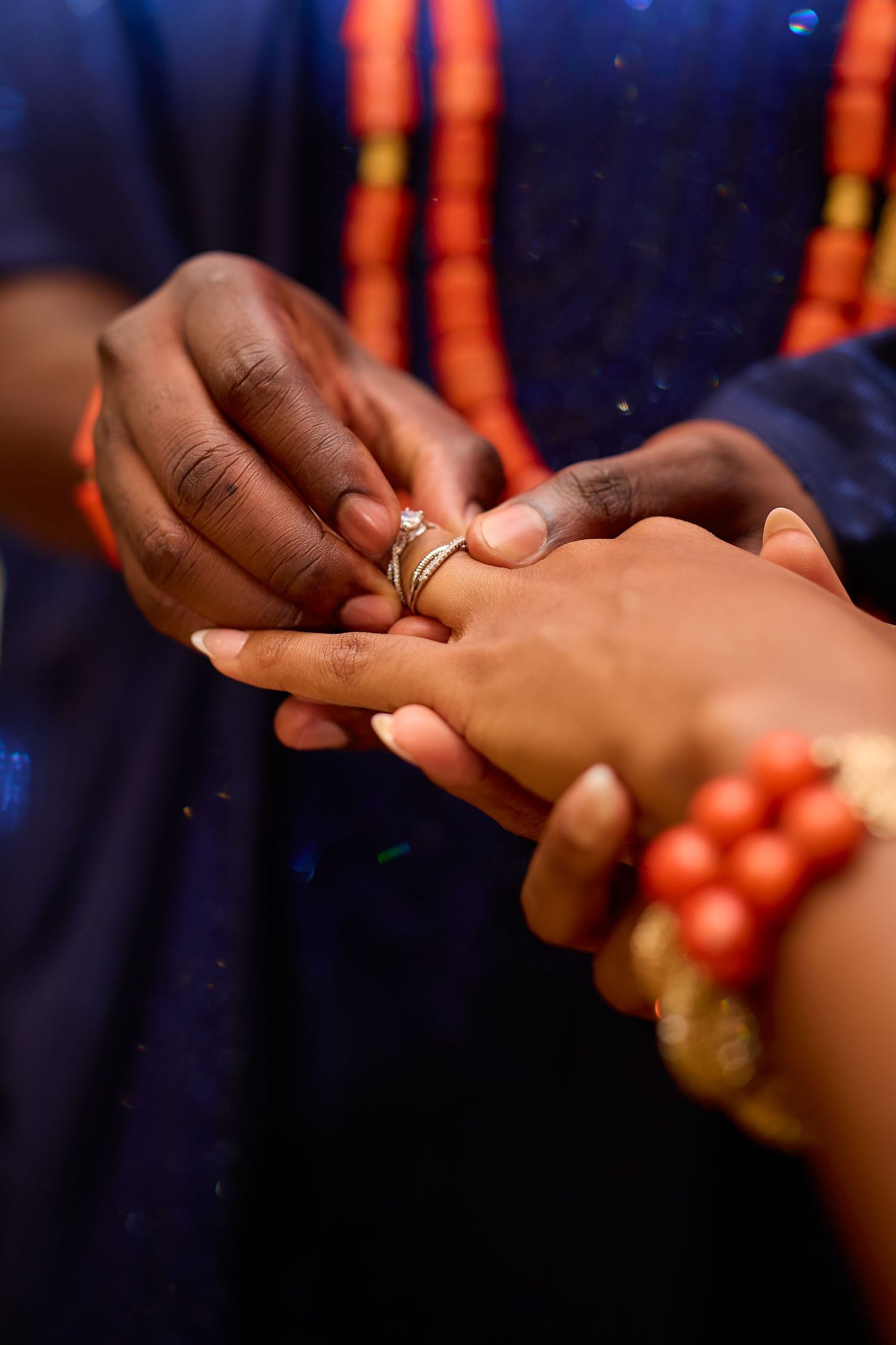 Man placing a gold diamond ring on a woman's finger during a traditional African wedding ceremony with coral bead jewelry.