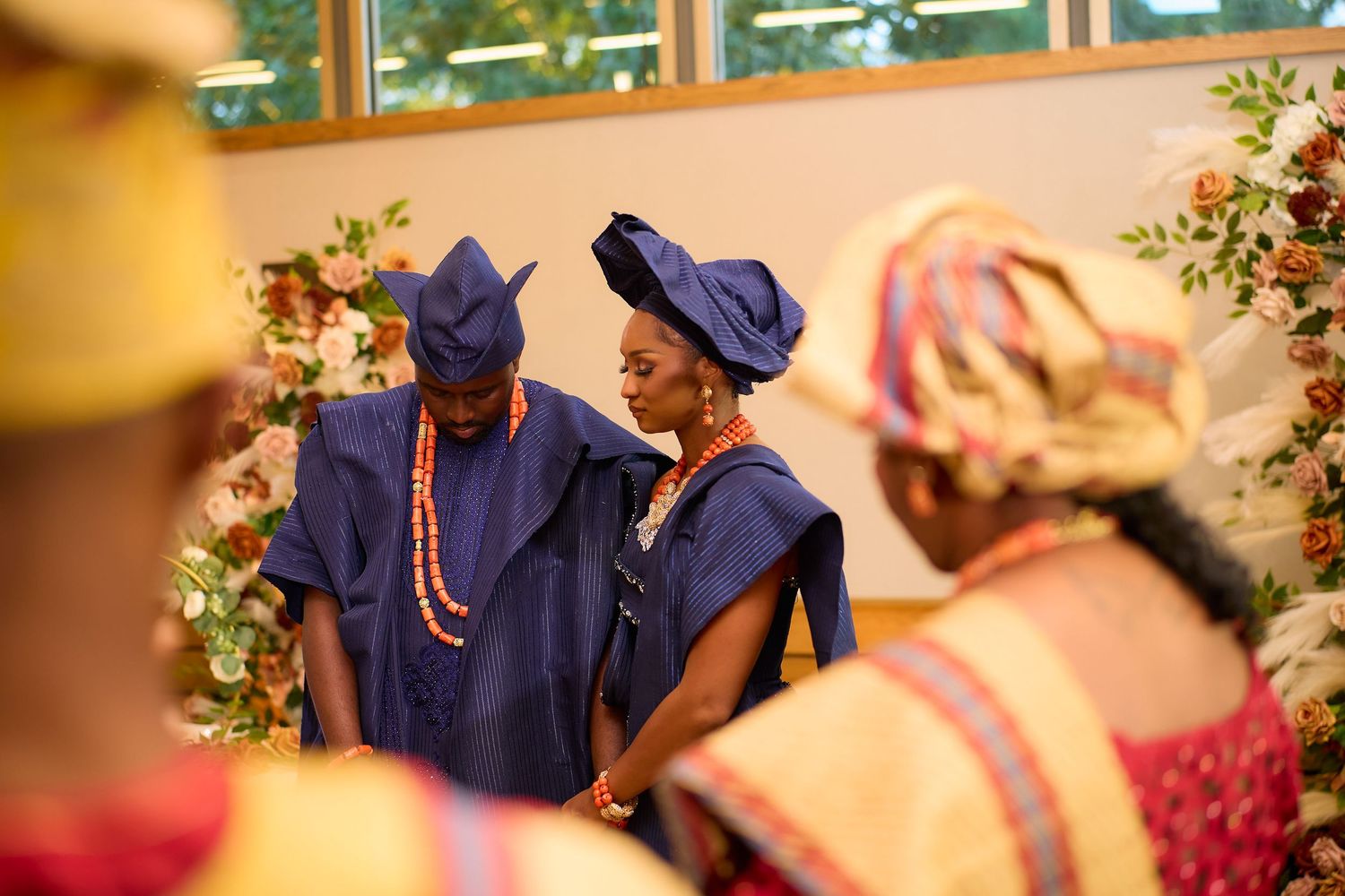 Couple in traditional Nigerian blue agbada attire at a colorful cultural wedding ceremony with floral decorations.