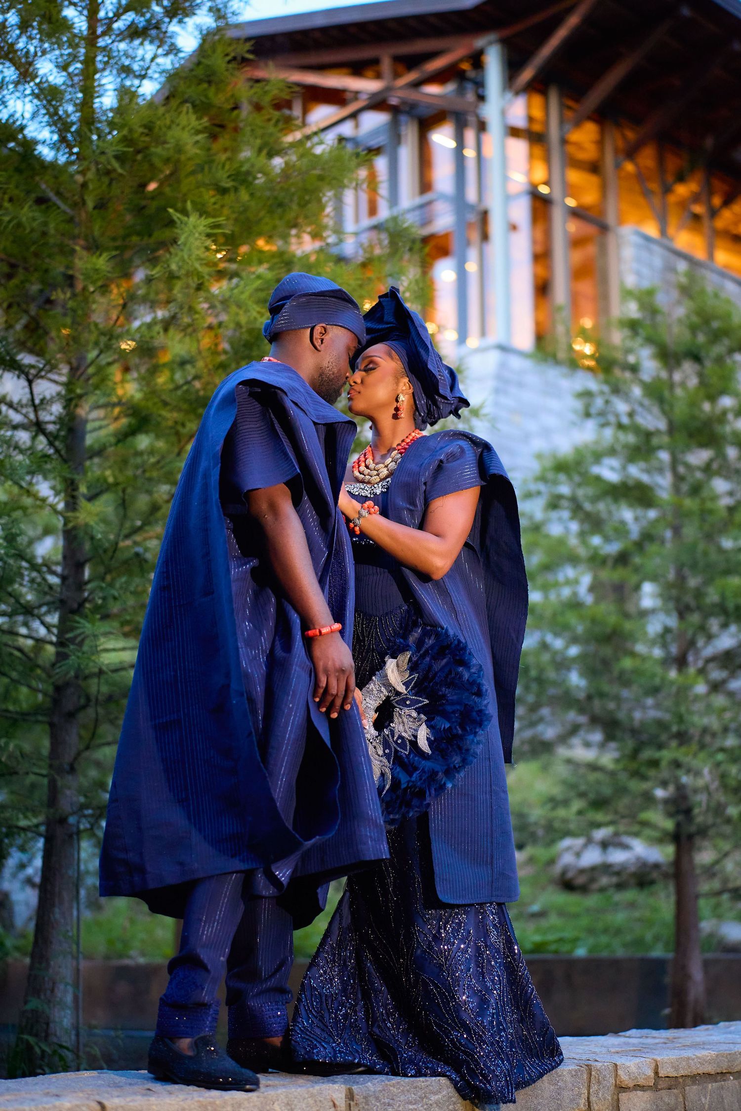 Couple in matching navy blue traditional African attire share a romantic moment outdoors at dusk.