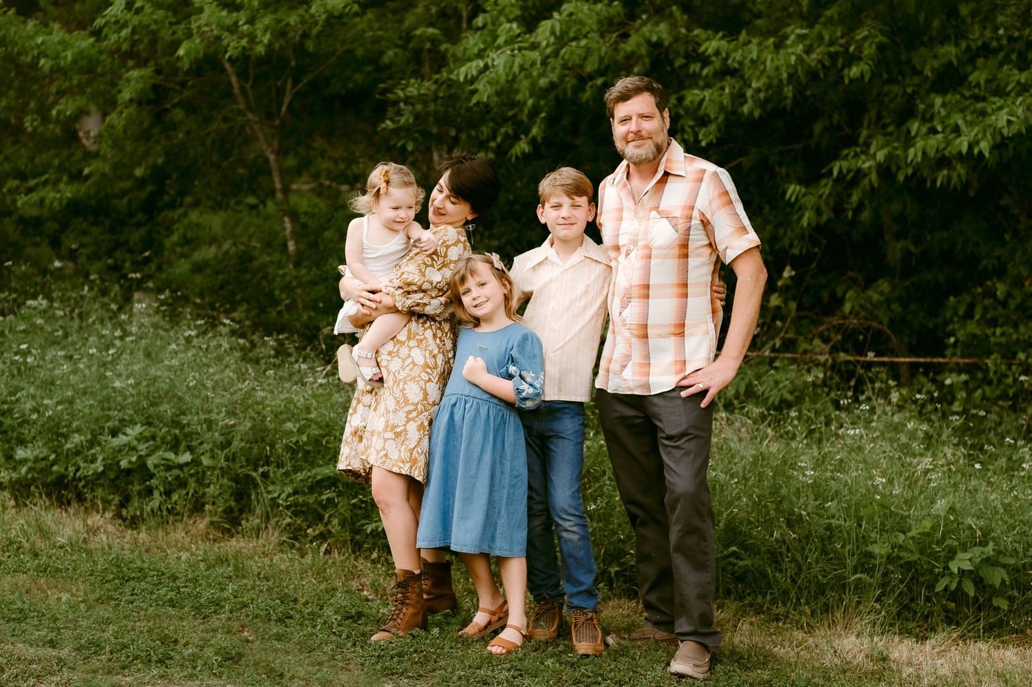 Family portrait outdoors in summer meadow with lush green foliage.
