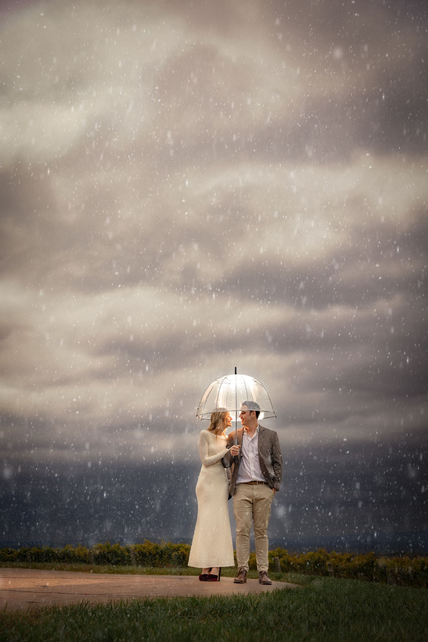 A couple shares an umbrella in a field as storm clouds gather and rain falls in this moody panoramic sequence.