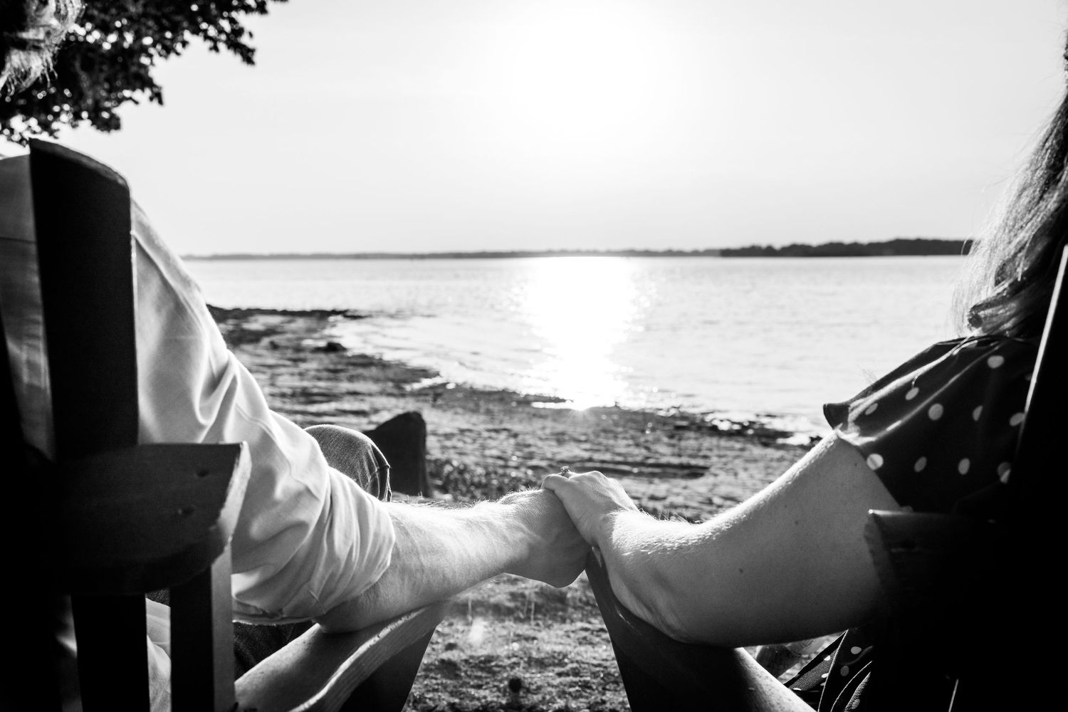 Black and white photo of two people relaxing in chairs overlooking a serene lake at sunset.