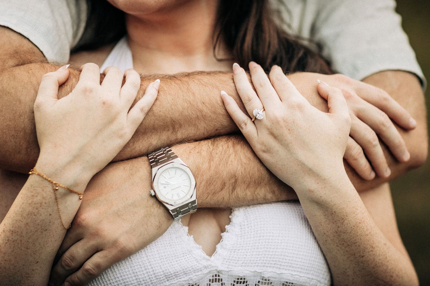 Close up of embracing hands with a silver watch visible against a tan sweater and white top.