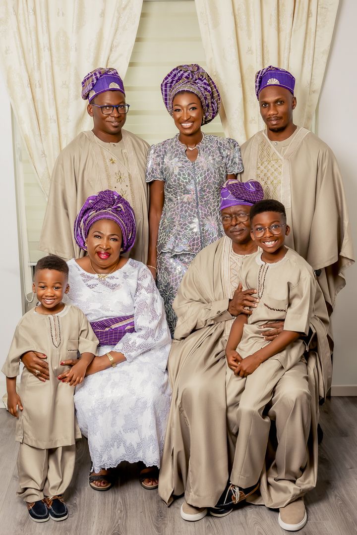 Traditional family portrait with members wearing coordinated Nigerian attire in purple and beige.