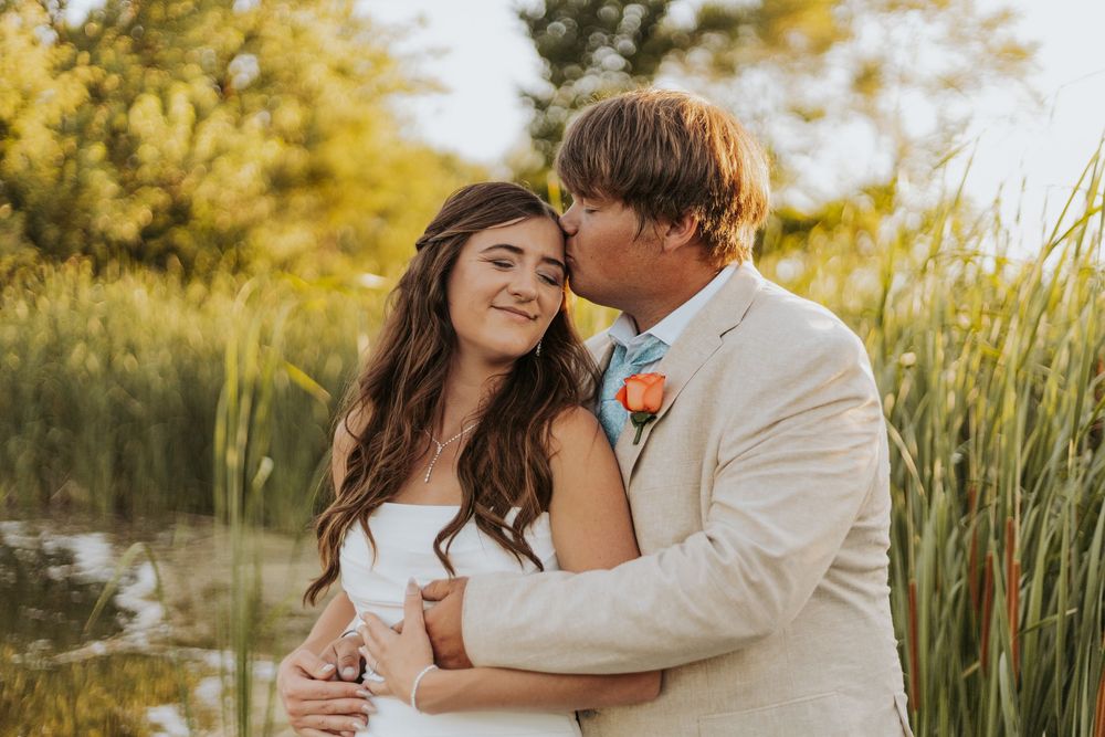 A couple shares a romantic moment in a golden sunlit field during a sunset photoshoot.