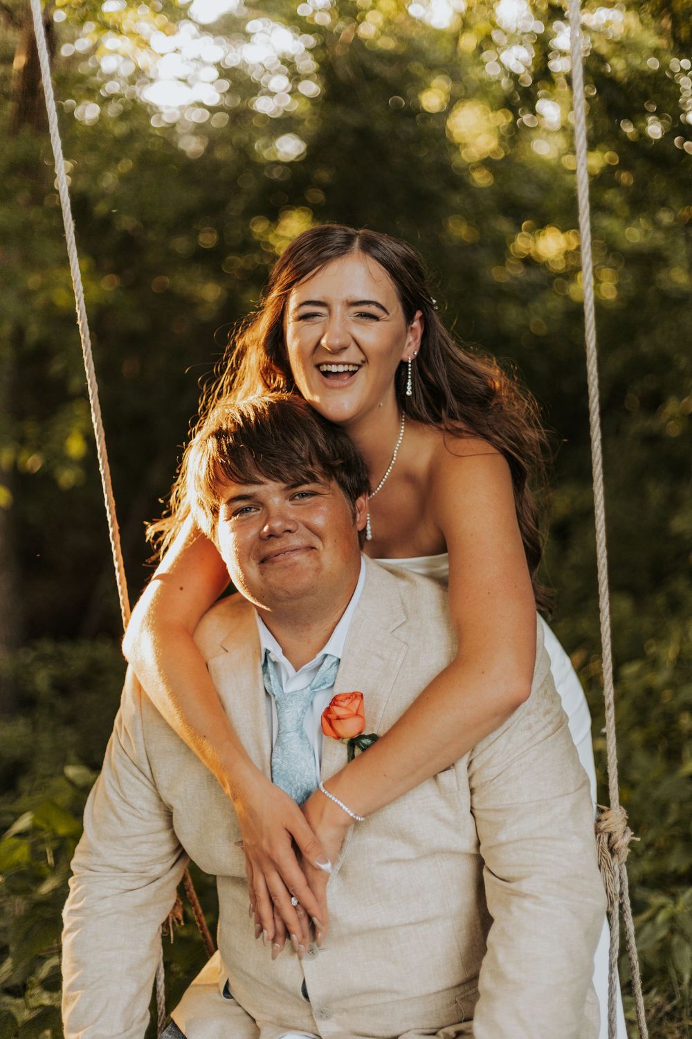 A couple shares a joyful moment together outdoors during golden hour while wearing light colored attire.