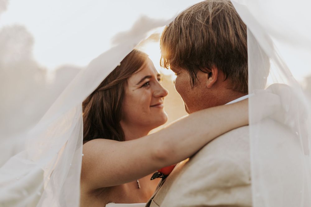 Intimate couple sharing tender moments together while lying in white bedding with soft natural lighting.