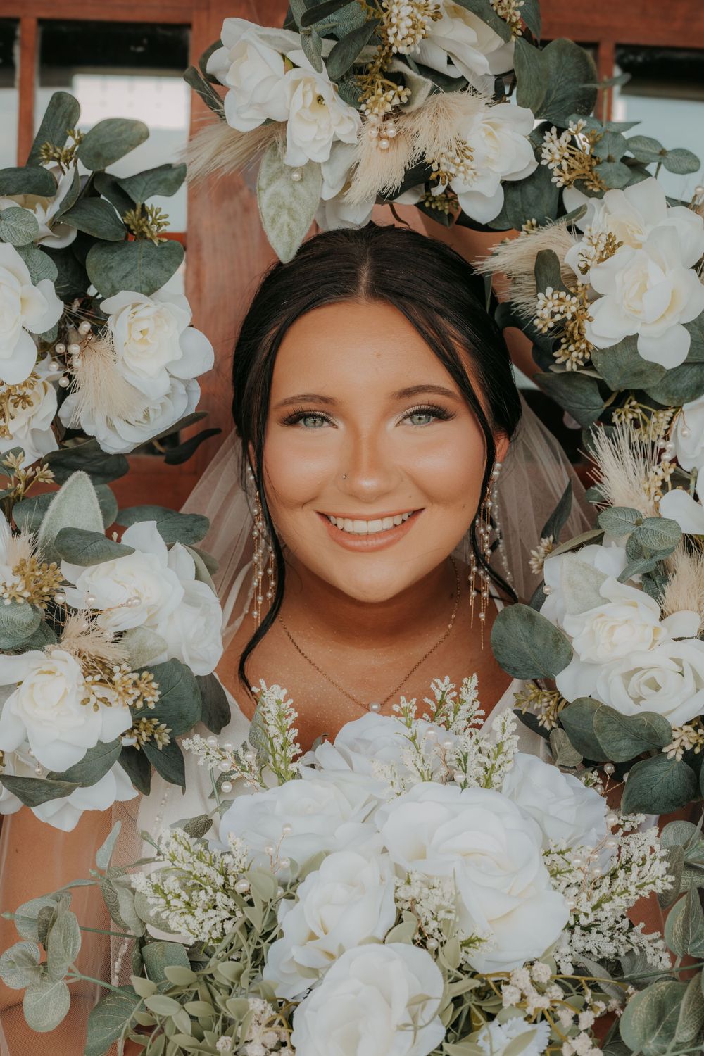 Bridal portrait framed by elegant white roses and greenery arch.