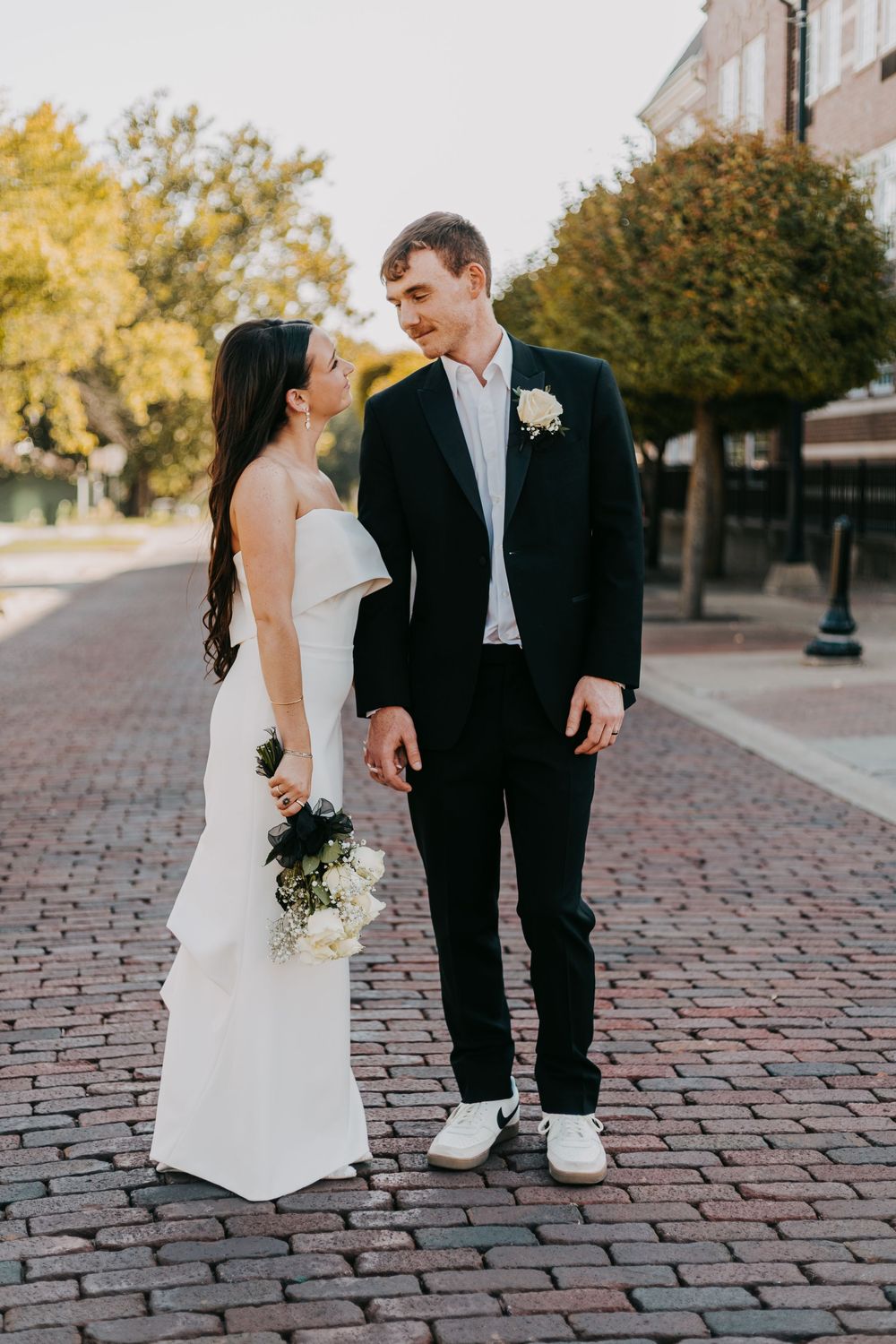 A bride and groom share playful moments on a brick paved street during their wedding photoshoot.