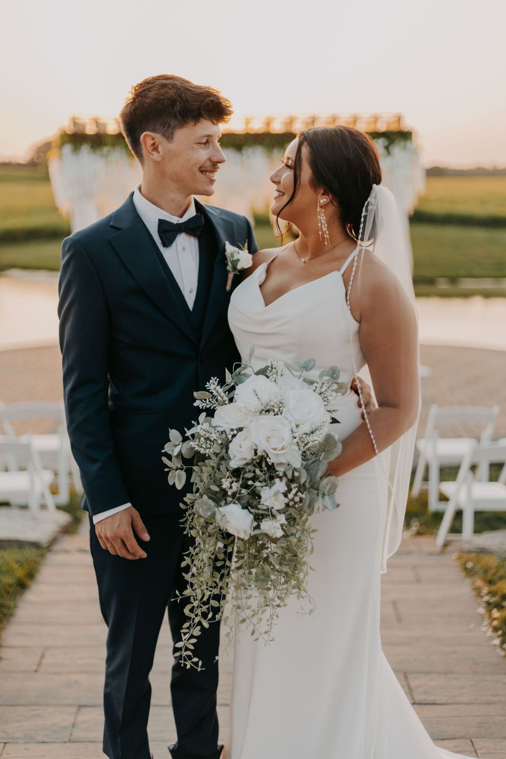Elegant outdoor wedding portrait with couple standing together holding white cascading bouquet.