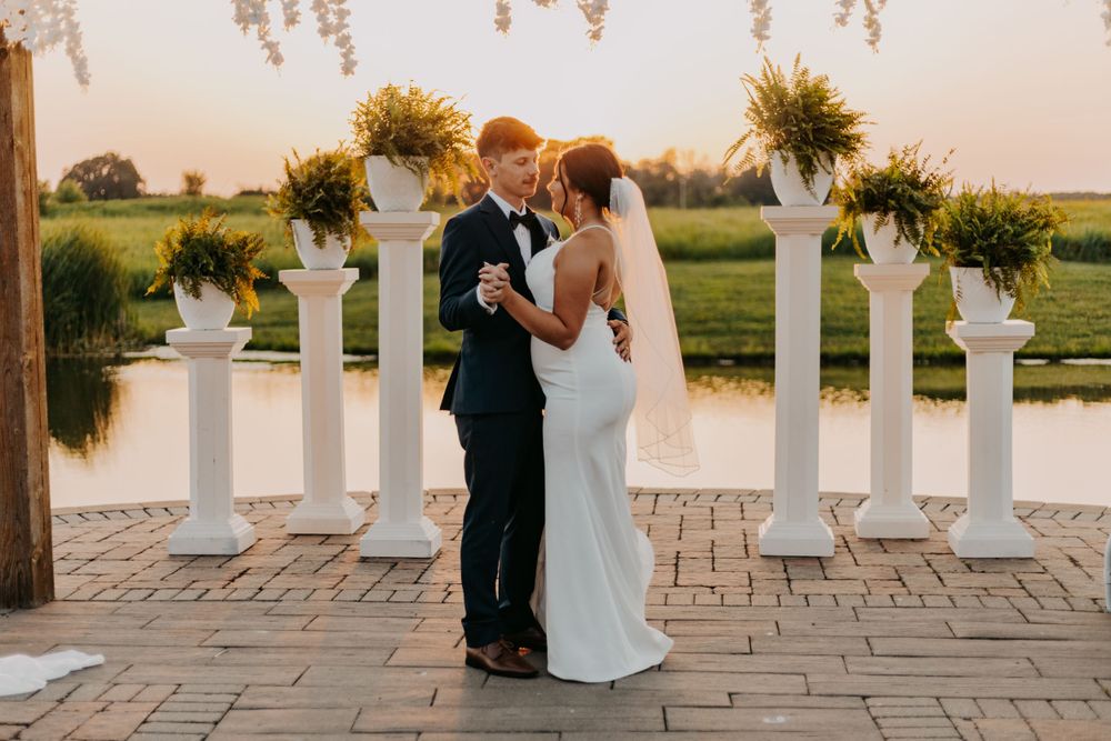 Wedding couple embracing by sunflower decorated pillars beside water feature at sunset.