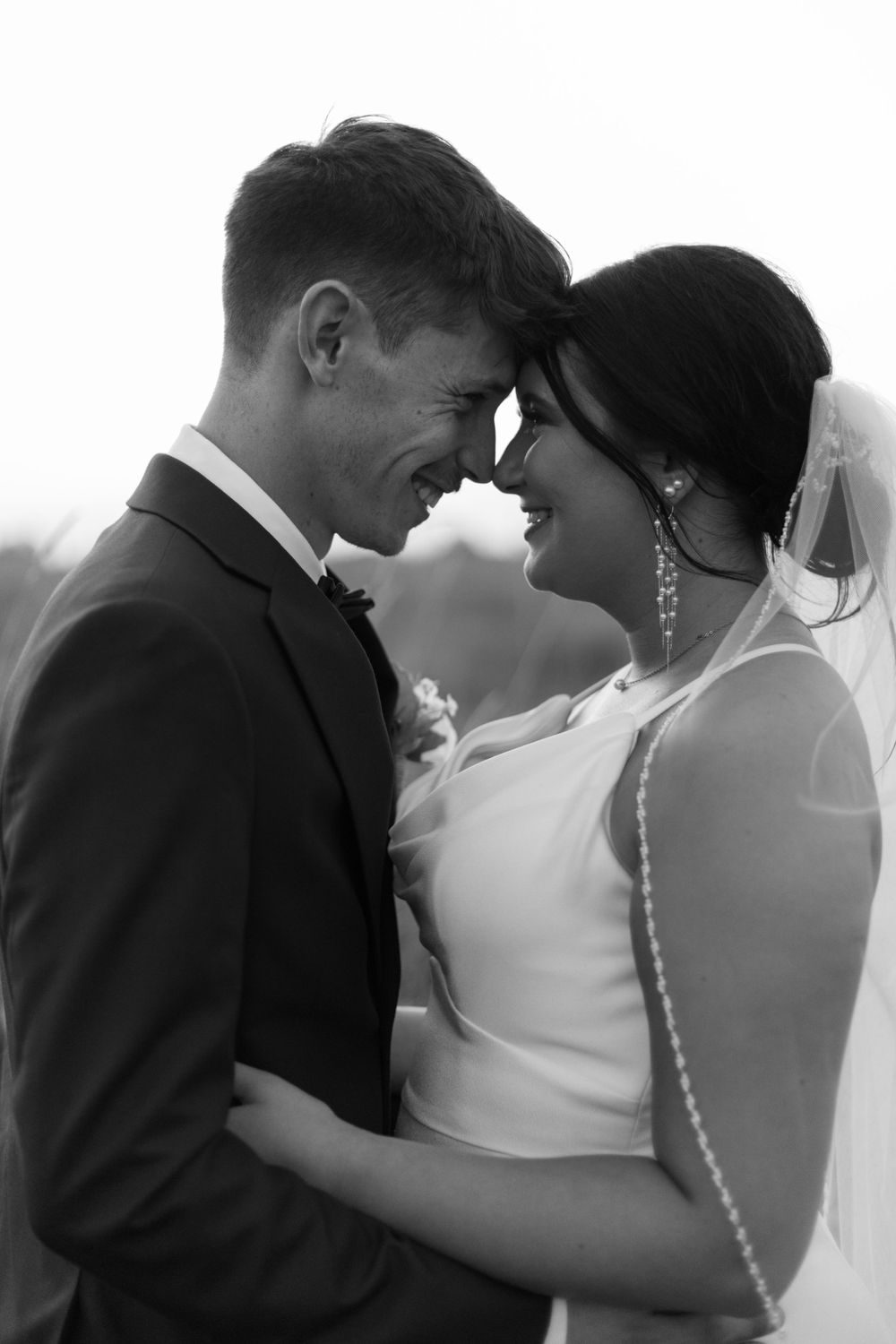 Black and white candid moment of newlyweds sharing laughter during their wedding.