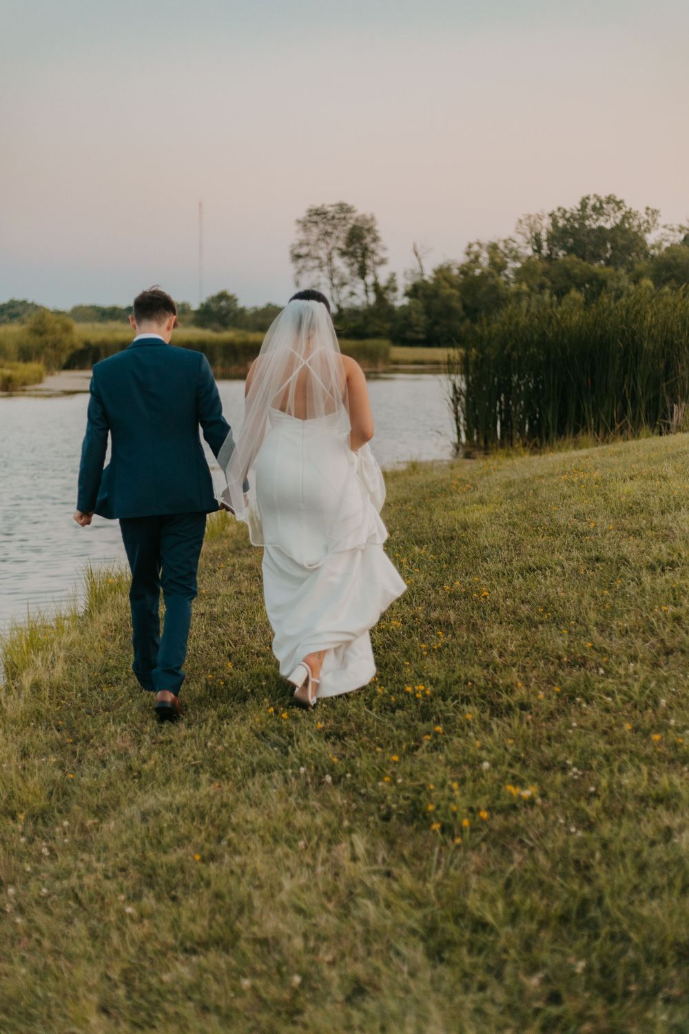 Bride and groom walking along a lakeside path during golden hour.
