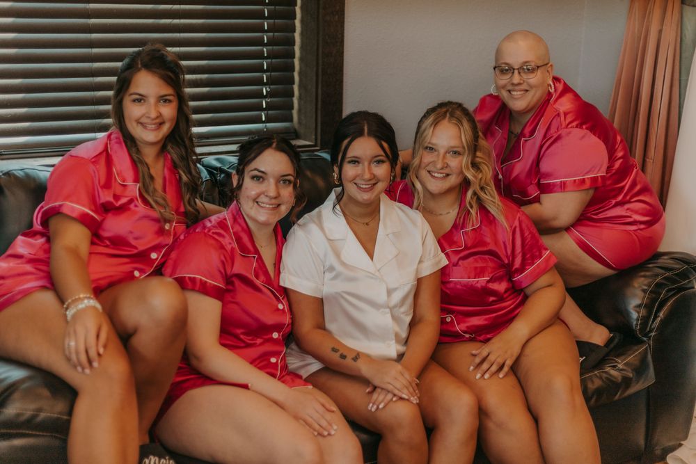 Group wearing matching pink satin robes sitting together on dark leather couch.