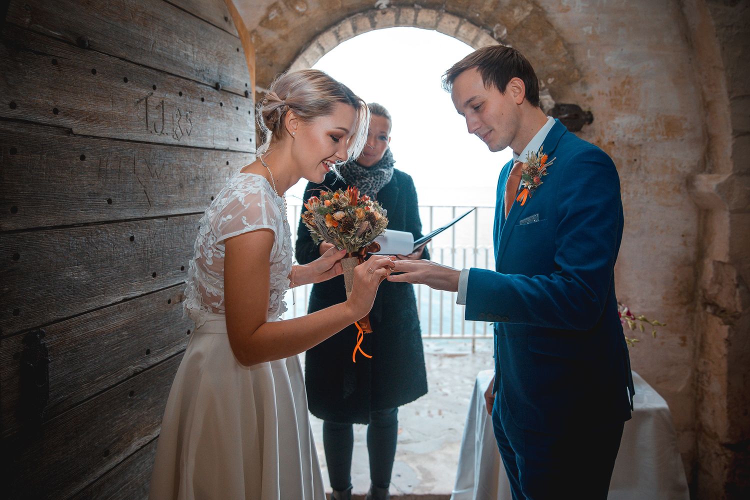 A romantic wedding moment between a couple in a rustic stone archway with a bouquet of flowers.