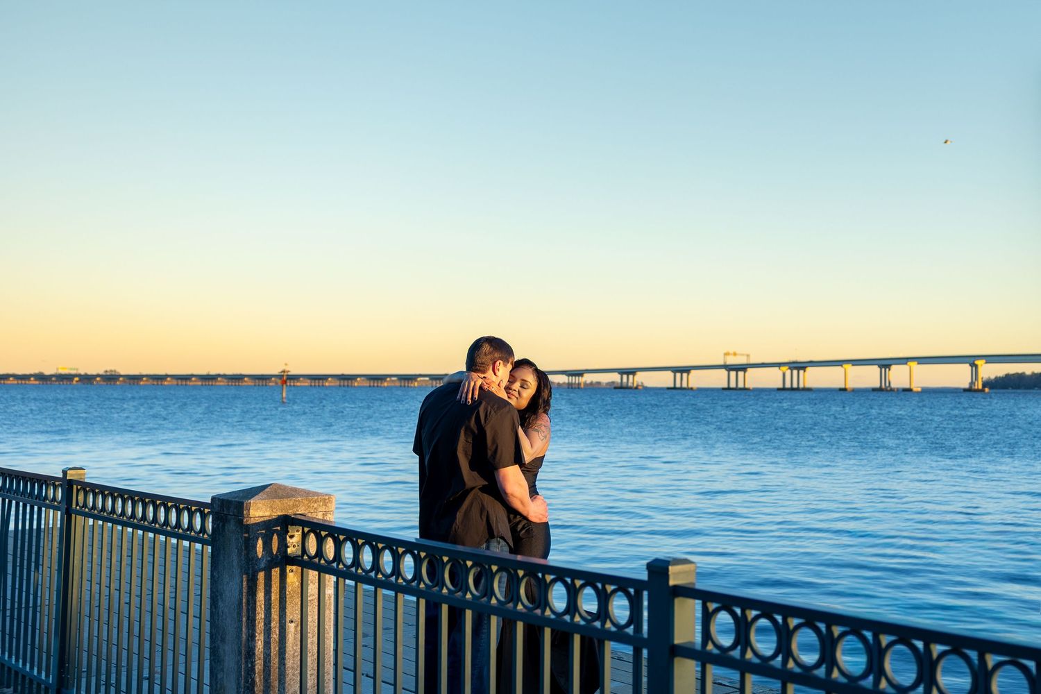 Couple sharing an intimate moment at sunset by a waterfront railing with ocean view (New Bern, NC).