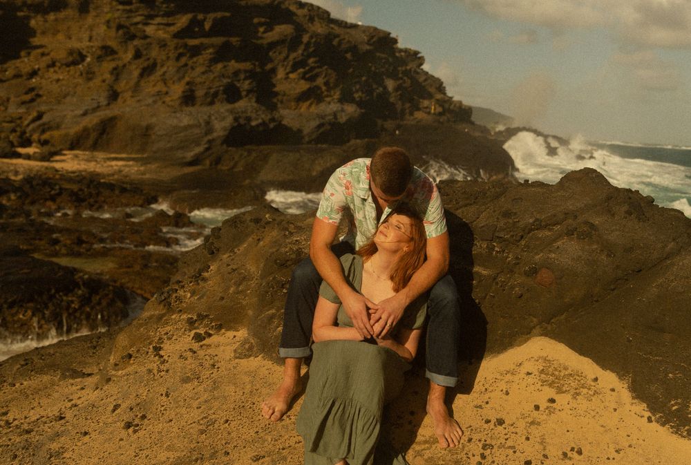 A romantic couple embracing on rocky coastal cliffs with ocean waves in the background.