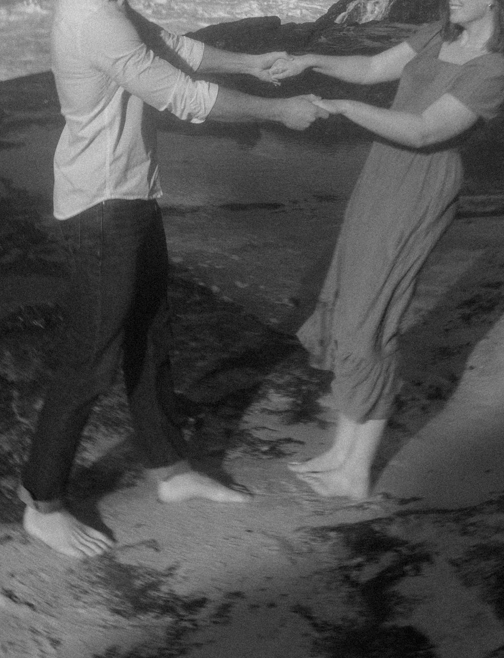 A black and white photo of a couple dancing together on a rocky beach.
