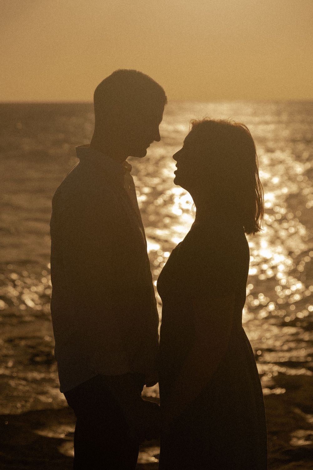 Silhouetted couple stands together against a sparkling sunset ocean view.