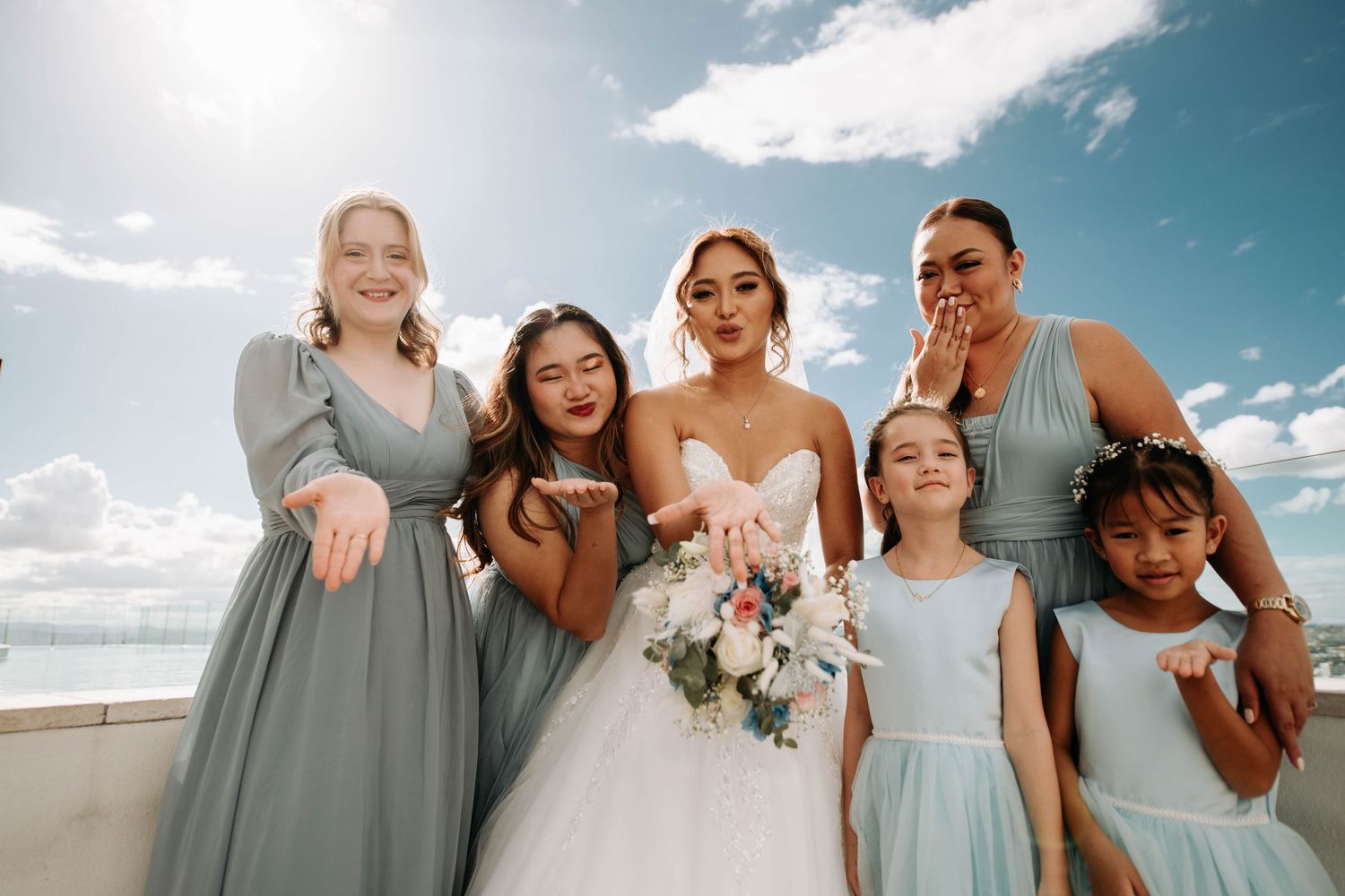 Wedding party in grey and light blue dresses pose together on a rooftop.