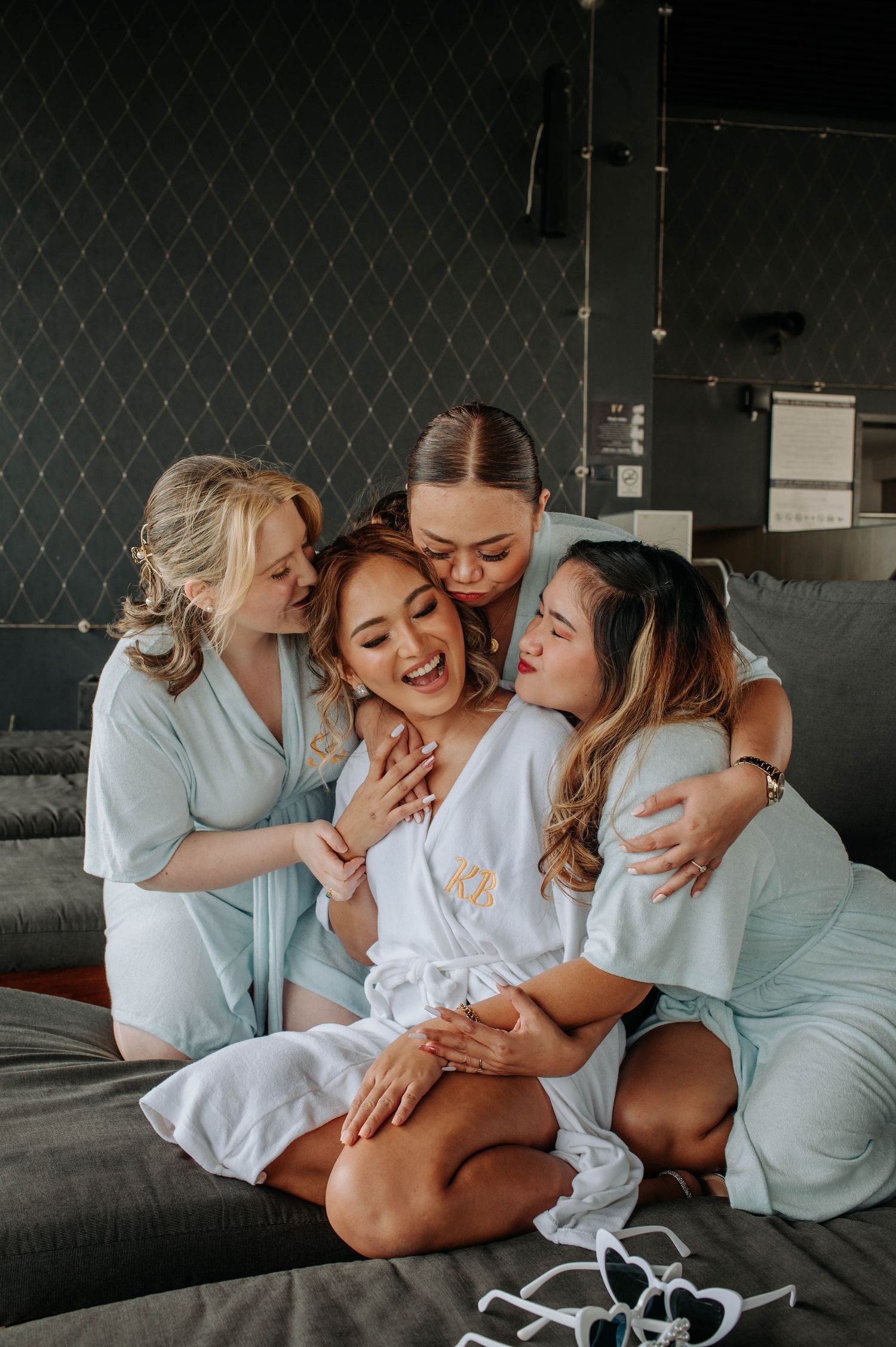 Friends in white robes share joyful moment together on grey couch.