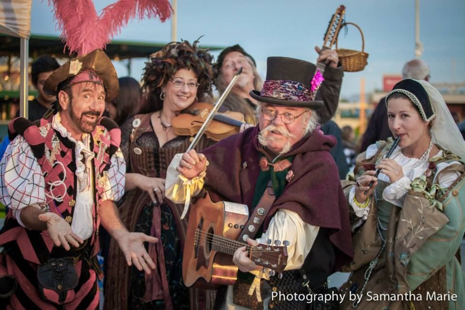 Costumed renaissance fair performers pose together with musical instruments and festive attire.