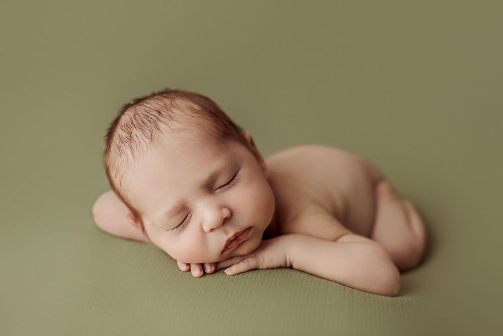 Peaceful sleeping newborn baby lying on soft olive green backdrop at his newborn session in Tulsa,OK
