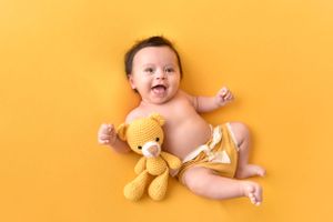 Happy baby posing with teddy bear on bright yellow background.