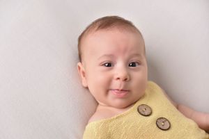 Baby wearing yellow button detail outfit against white background.