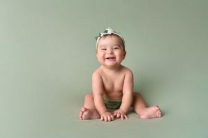 Smiling baby in green outfit during professional milestone photo session.