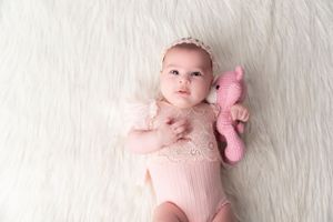 Baby portrait session on white furry backdrop with pink accessories.