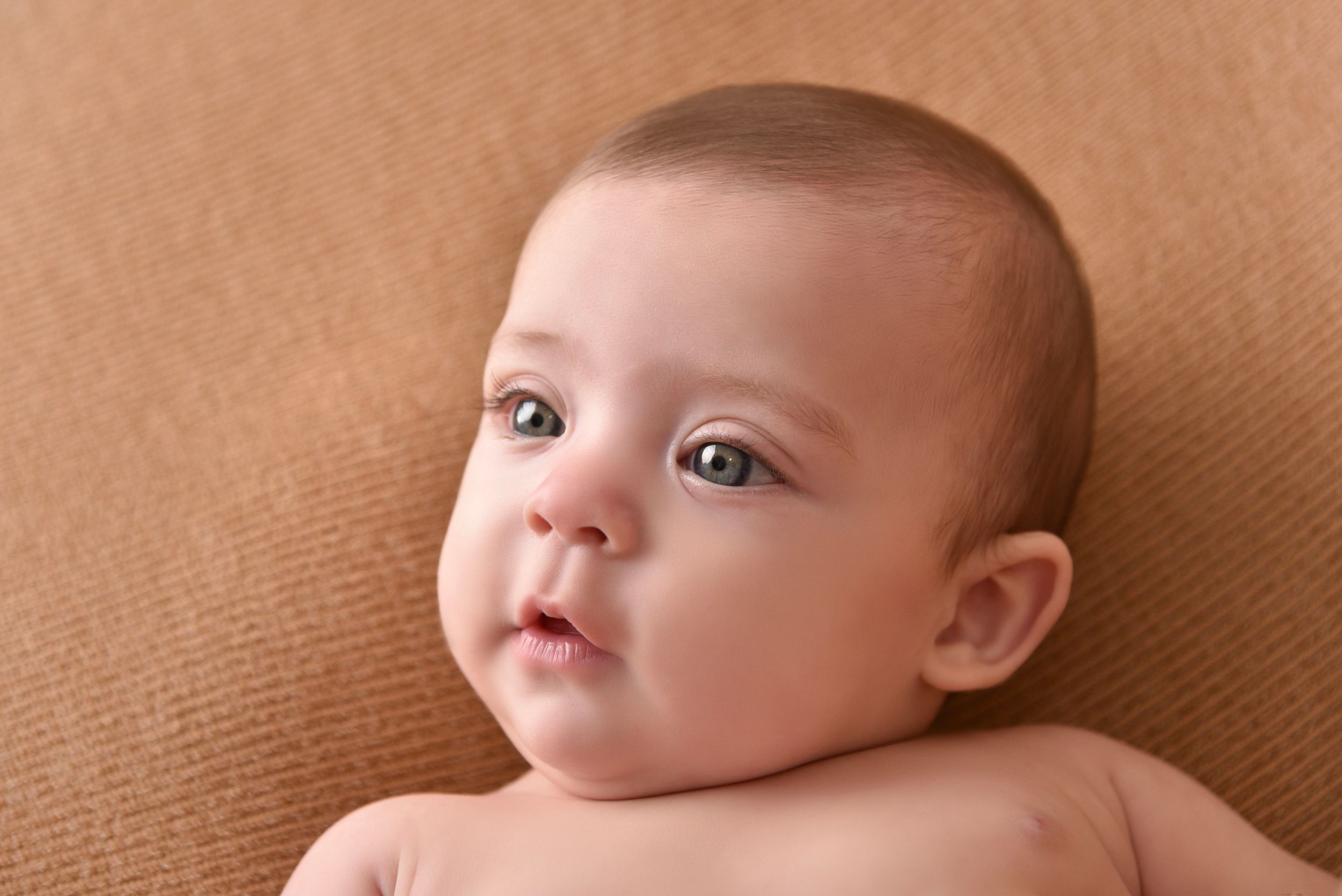 Close-up portrait of baby against warm brown backdrop.