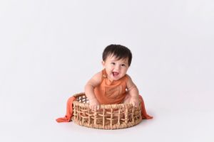 Playful baby posing with wooden birthday cake prop on white background.