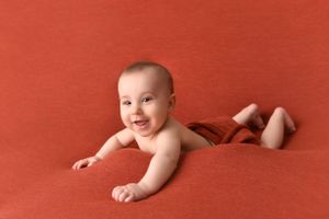 Baby lying on bright orange backdrop with happy expression during photoshoot.