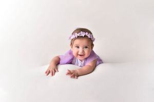 Baby wearing floral crown lying on stomach during professional photo shoot.