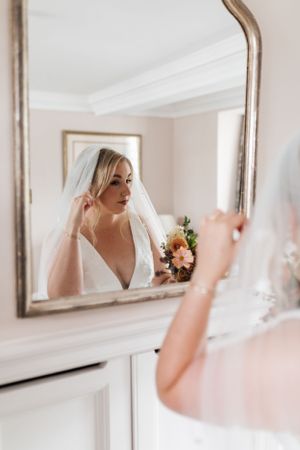 Reflection in vintage mirror shows wedding preparations with white veil and peach bouquet.