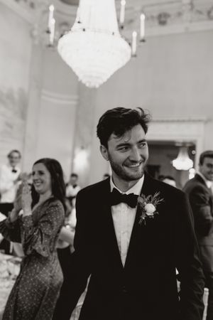 Black and white photo of reception guest in tuxedo under crystal chandelier.