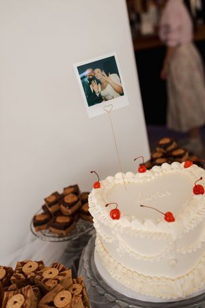 White wedding cake decorated with cherries and photo toppers displayed alongside chocolate desserts.