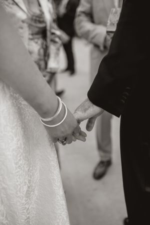 Black and white wedding photo showing hands and dress details during intimate ceremony moment.