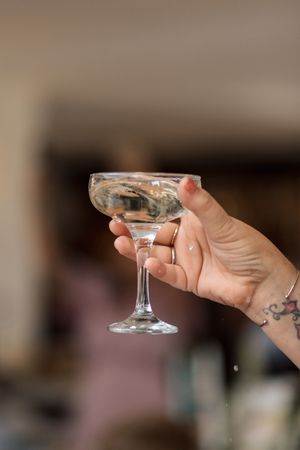 Hand holding vintage champagne coupe glass showing wedding ring detail.