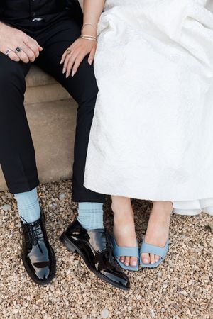 A detail shot of wedding footwear showing formal black shoes and blue sandals on a light-colored carpet.