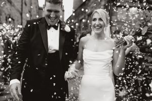 Black and white photo of a couple laughing in a shower of confetti at their wedding celebration.