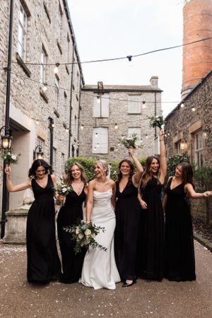 Wedding party poses together in an industrial stone courtyard with string lights overhead.