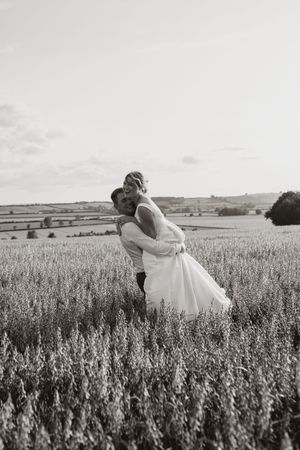 Black and white photo of a couple embracing in a serene wheat field during a romantic outdoor photoshoot.